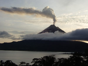 The Arenal Vlcano eits a huge plume as the sun comes up behind it. 